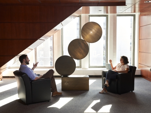Two students sit apart in a sunlit area talking